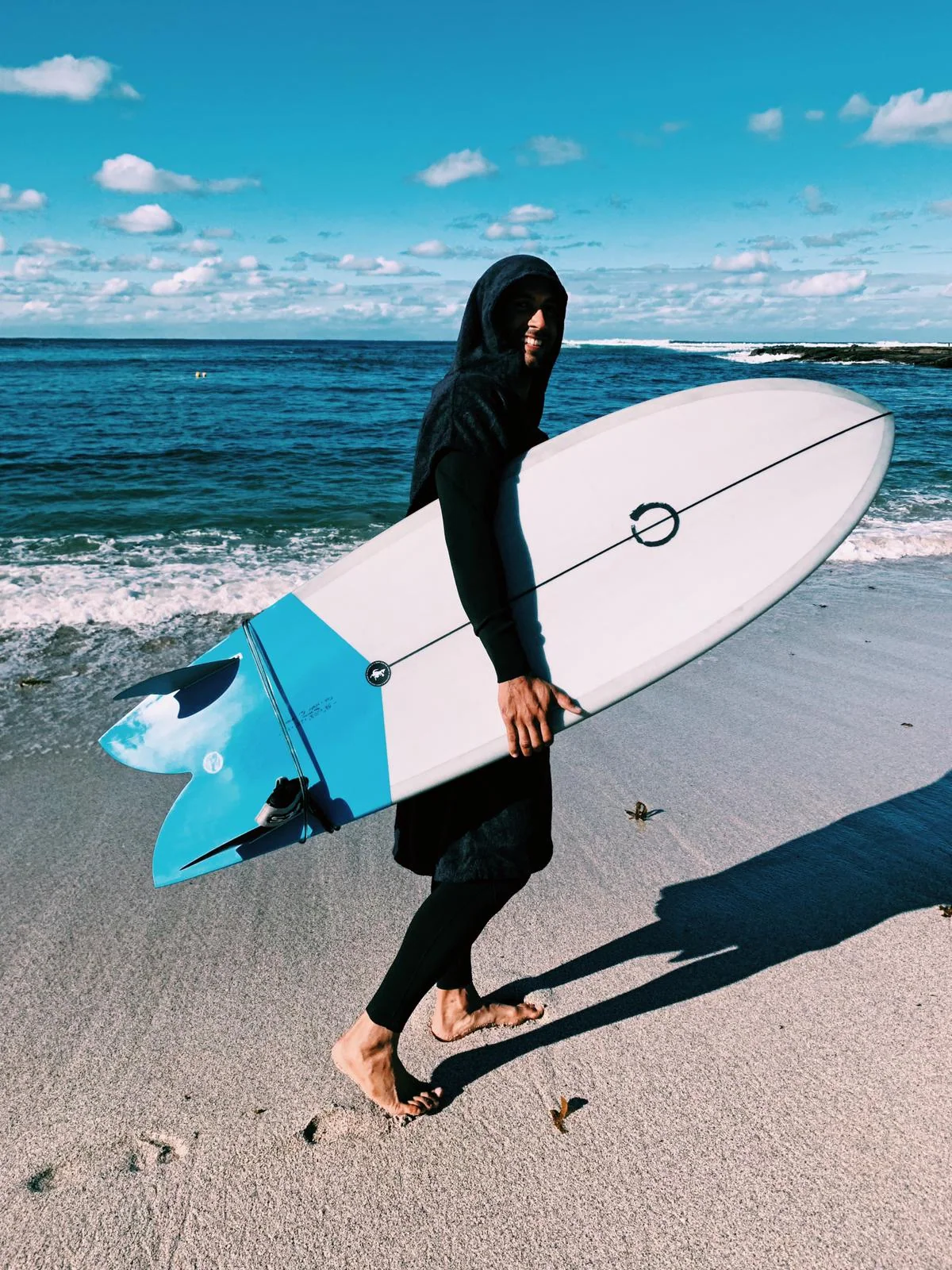 Surfer arriving at the beach with a blue Yugen twin-fin