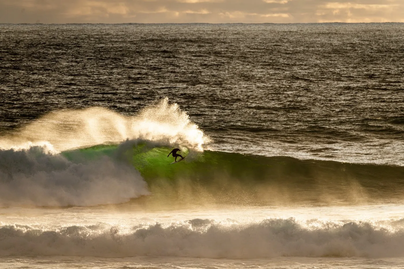 Surfer driving through a bottom turn at sunrise